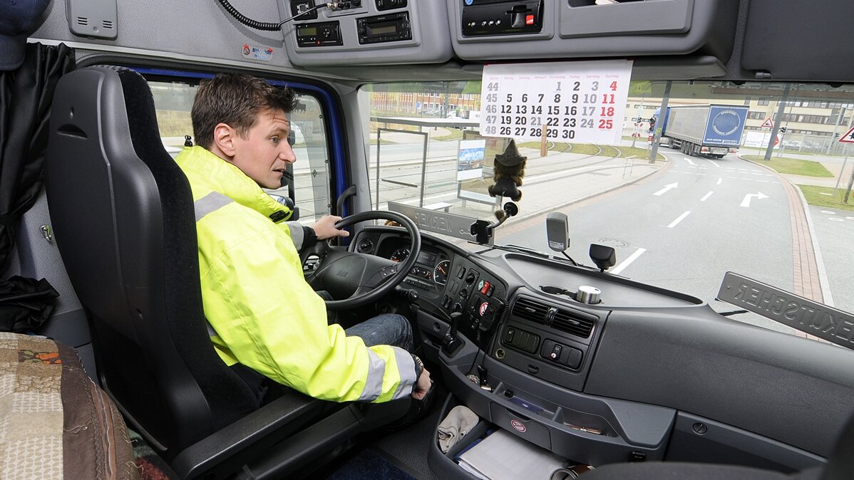 Ein Mann in Warnweste sitzt am Steuer eines Lastkraftwagens.