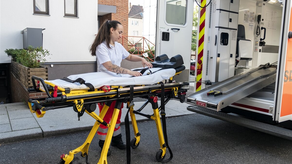 Eine junge Frau schiebt eine Trage in einen Krankenwagen.