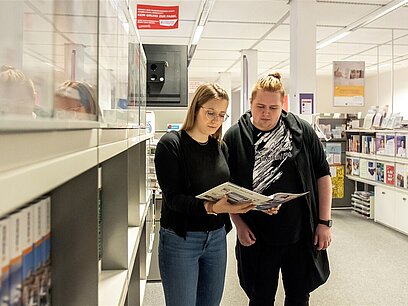 Eine junge Frau und ein junger Mann lesen in einem Heft im Berufsinformationszentrum. 