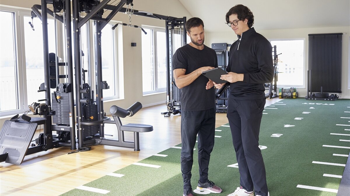Ben-Luca und ein Trainer arbeiten am Tablet im Fitnessraum.