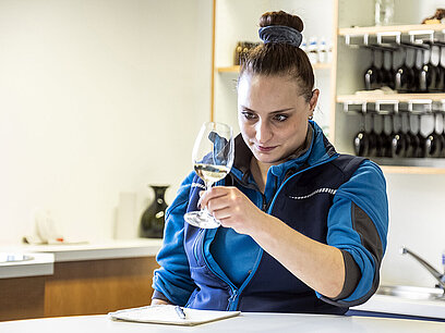 Eine junge Frau beurteilt die Klarheit eines Weins in einem Glas. 