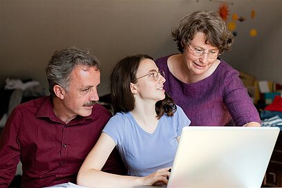 Eine junge Frau sitzt mit ihren Eltern vor einem Laptop.