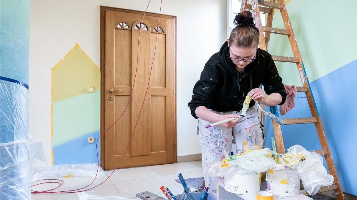 Eine junge Frau in Arbeitskleidung für Maler streicht Farbe auf einen Farbroller.