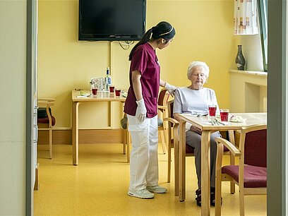 Eine junge Frau hilft einer älteren Frau in einem Pflegeheim beim Frühstück.
