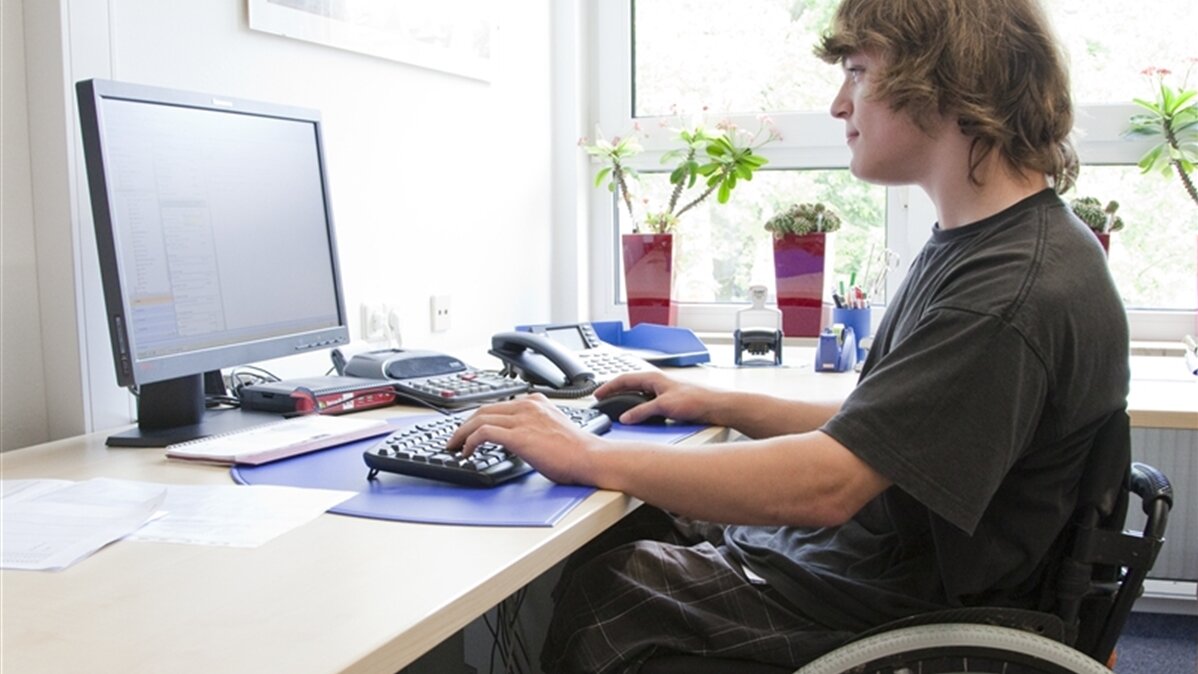 Ein junger Mann im Rollstuhl sitzt vor einem Computer.