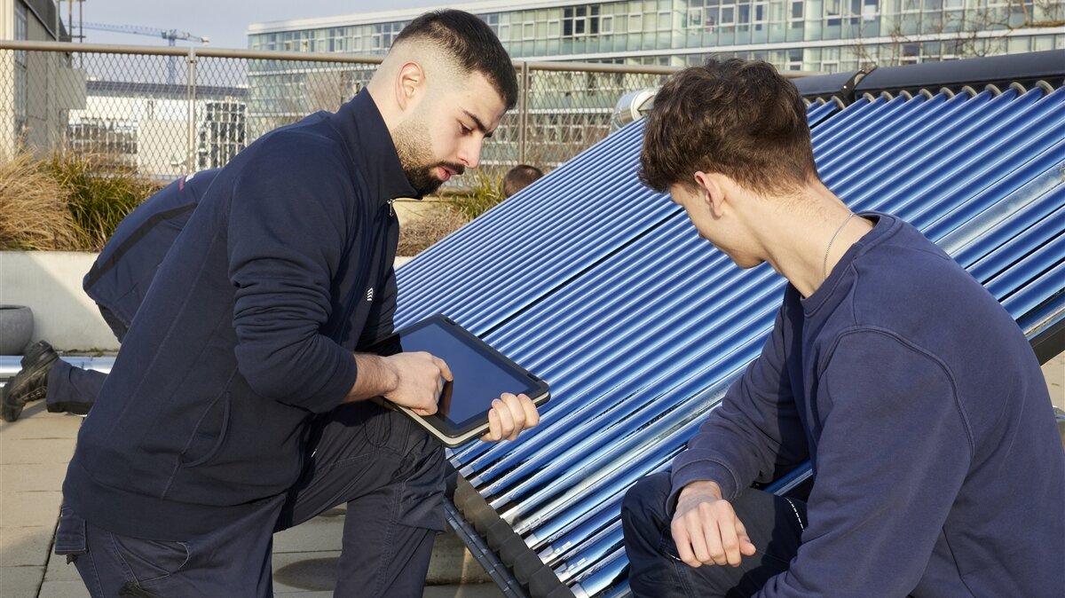 Zwei junge Männer arbeiten an einer Photovoltaikanlage und besprechen sich mit einem Tablet.