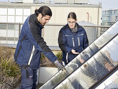 Ein Mann und eine Frau prüfen Solarzellen auf einem Dach.