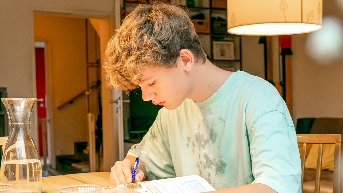 Ein junger Mann sitzt zuhause am Tisch und lernt.