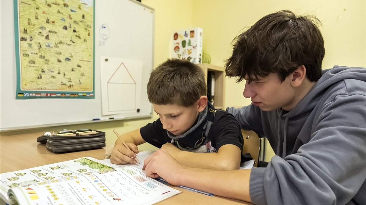 Ein Jugendlicher hilft einem Jungen bei den Hausaufgaben.