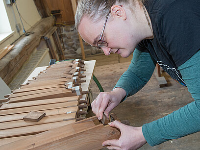 Eine Frau befestigt einen kleinen Holzklotz an einem Orgelbauteil.