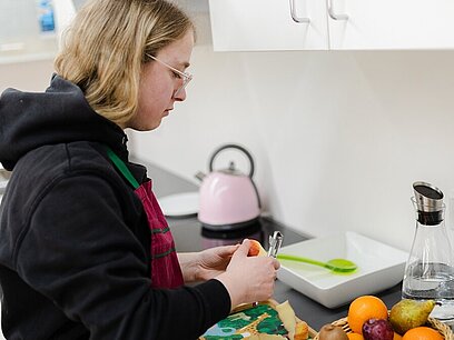 Eine junge Frau mit Schürze schält einen Apfel in einer Küche.