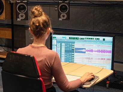 Eine junge Frau bearbeitet Tonspuren am Computer.