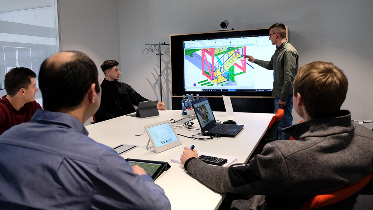 Martin präsentiert seinen Kollegen an einem großen Bildschirm ein 3-D-Modell.