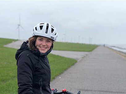 Eine Frau sitz auf einem Fahrrad mit Helm und sieht in die Kamera.