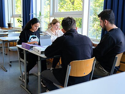 Eine Gruppe von vier jungen Menschen sitzt an einem Tisch und bereiten sich auf eine Prüfung vor.
