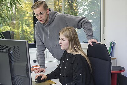 Ein junger Mann und eine junge Frau schauen gemeinsam auf einen Computer-Bildschirm.