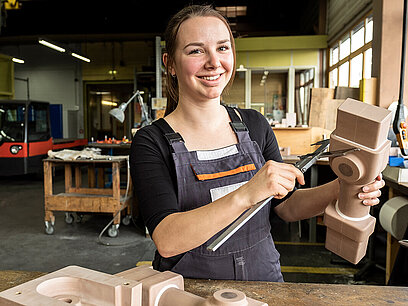 Eine junge Frau misst mit einem Messschieber die Maße eines Bauteils aus Holz nach.