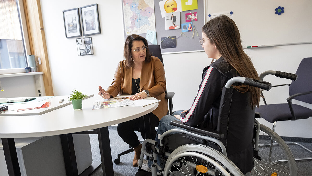 Eine Frau spricht mit einer Jugendlichen, die im Rollstuhl sitzt.
