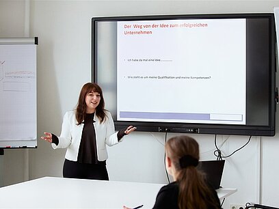 Eine junge Frau präsentiert vor ihrer Kollegin ihre Ideen an einem großen Bildschirm.