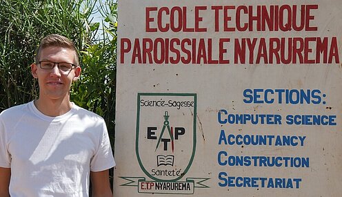 Felix steht neben einem Schild seiner Schule in Ruanda.