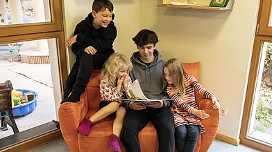 Ein junger Mann liest drei Kindern in einer Kindertagesstätte vor.