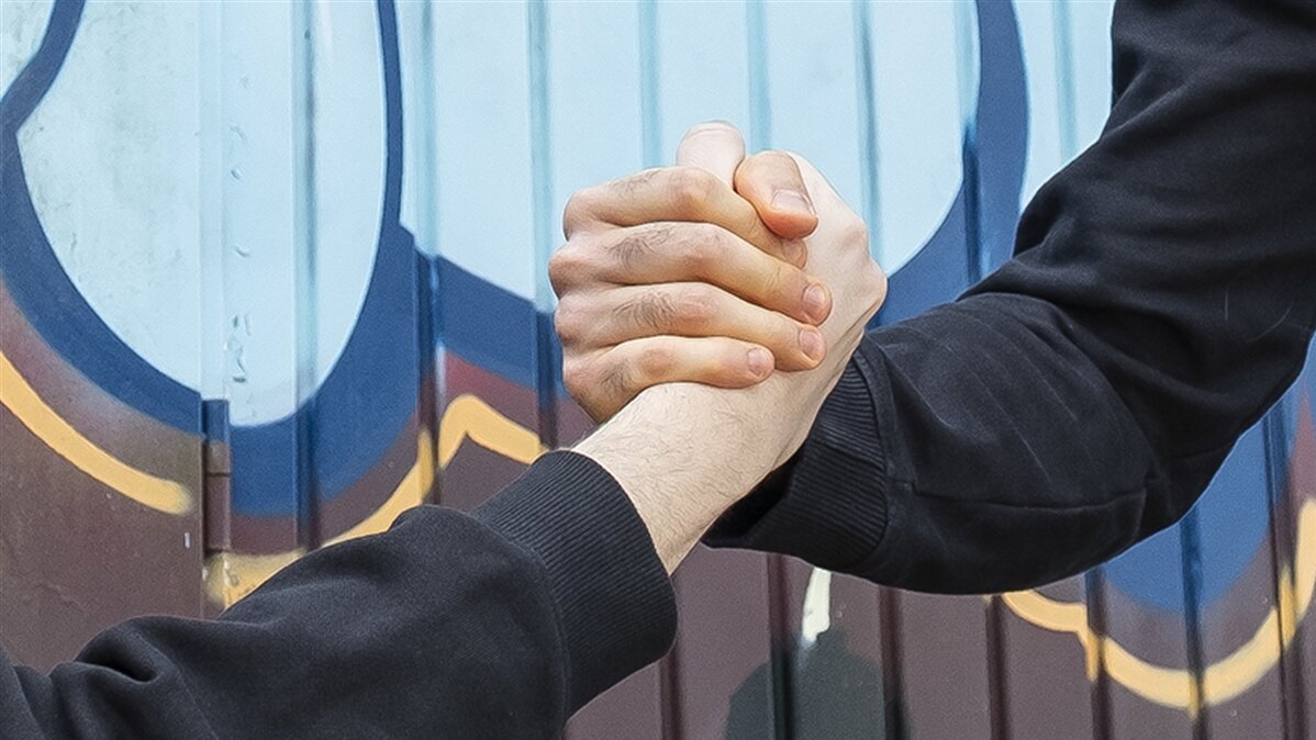 Ein Händedruck von zwei Männern vor einem mit Farbe besprühten Hintergrund.