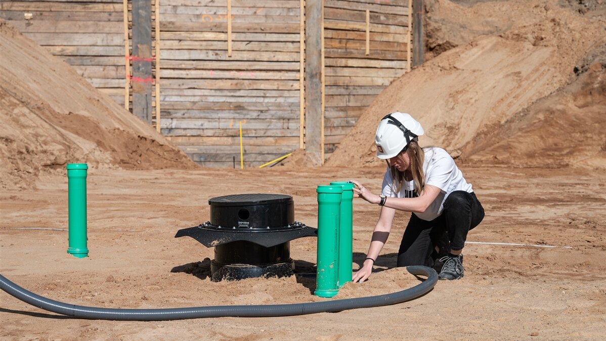 Eine junge Frau mit Schutzhelm arbeitet an einem Rohrsystem auf der Baustelle.