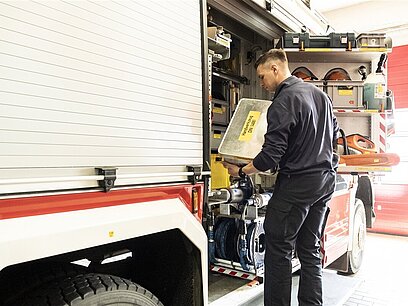 Ein junger Mann verlädt Material in ein Feuerwehrauto.