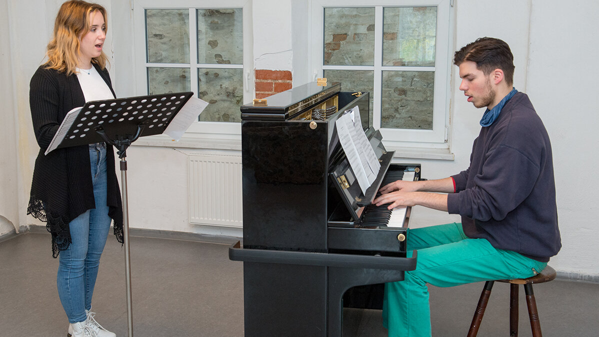Ein junger Musiklehrer begleitet seine Gesangsschülerin am Klaiver.