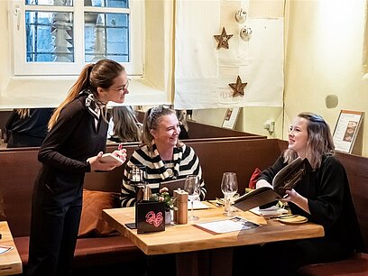 Eine junge Frau nimmt im Restaurant die Bestellung von zwei Frauen auf.