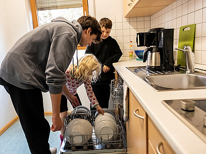 Zwei Jungen und ein Mädchen räumen die Spülmaschine aus.