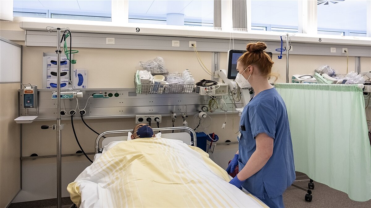 Eine Frau in OP-Kleidung beobachtet einen schlafenden Patienten.