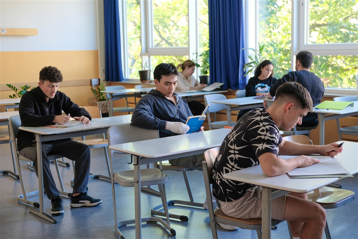 Mehrere Schüler und Schülerinnen sitzen an ihren Tischen in einem Klassenzimmer.