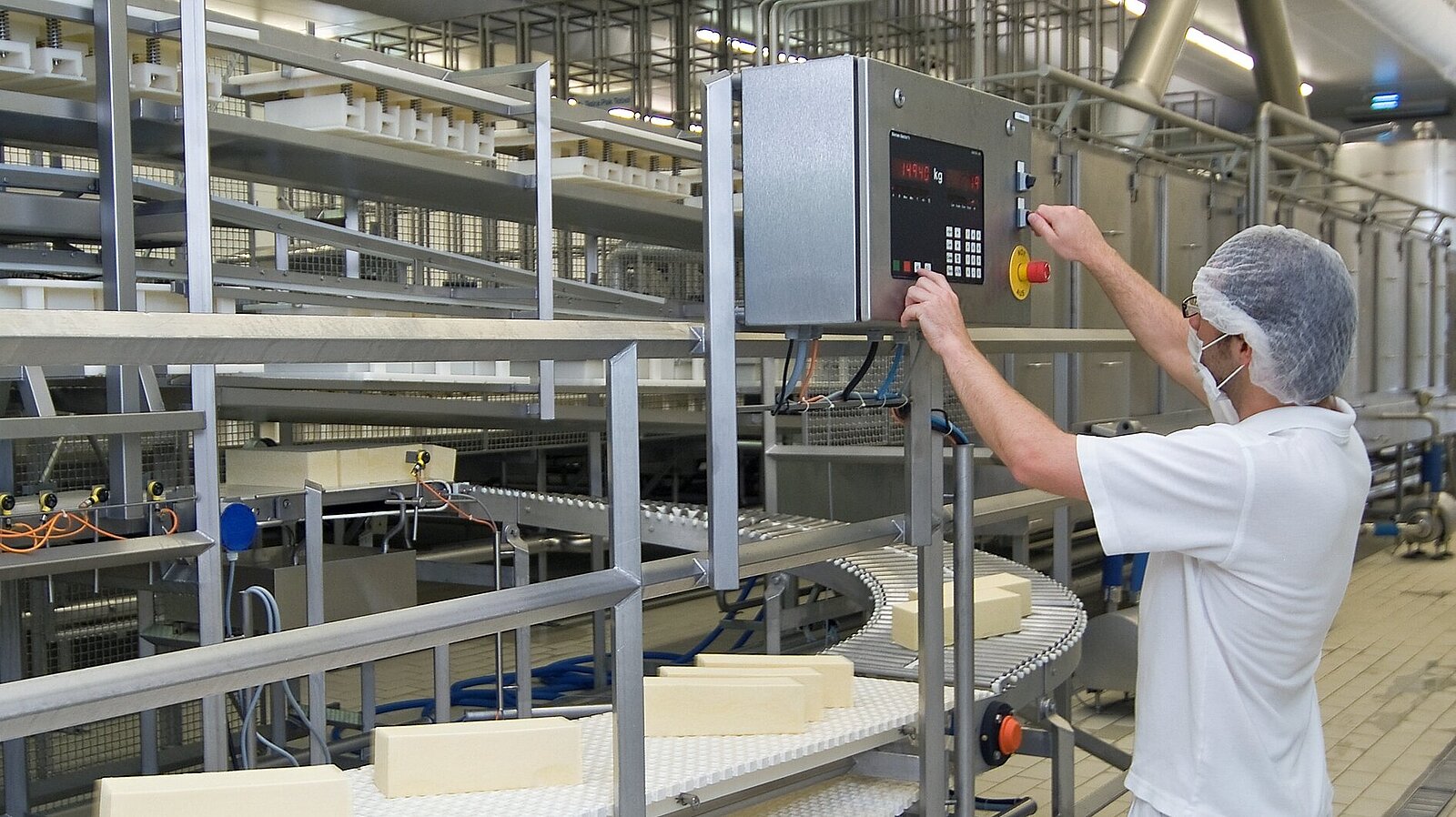 Ein Mitarbeiter stellt die Produktionsbänder für die Käseherstellung ein.