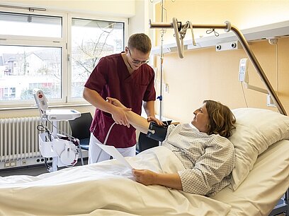 Ein junger Pfleger misst den Blutdruck einer Patientin in einem Krankenbett.