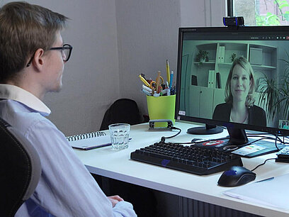 Ein junger Mann sitzt vor einem Computer und nimmt an einem Video-Vorstellungsgespräch teil.