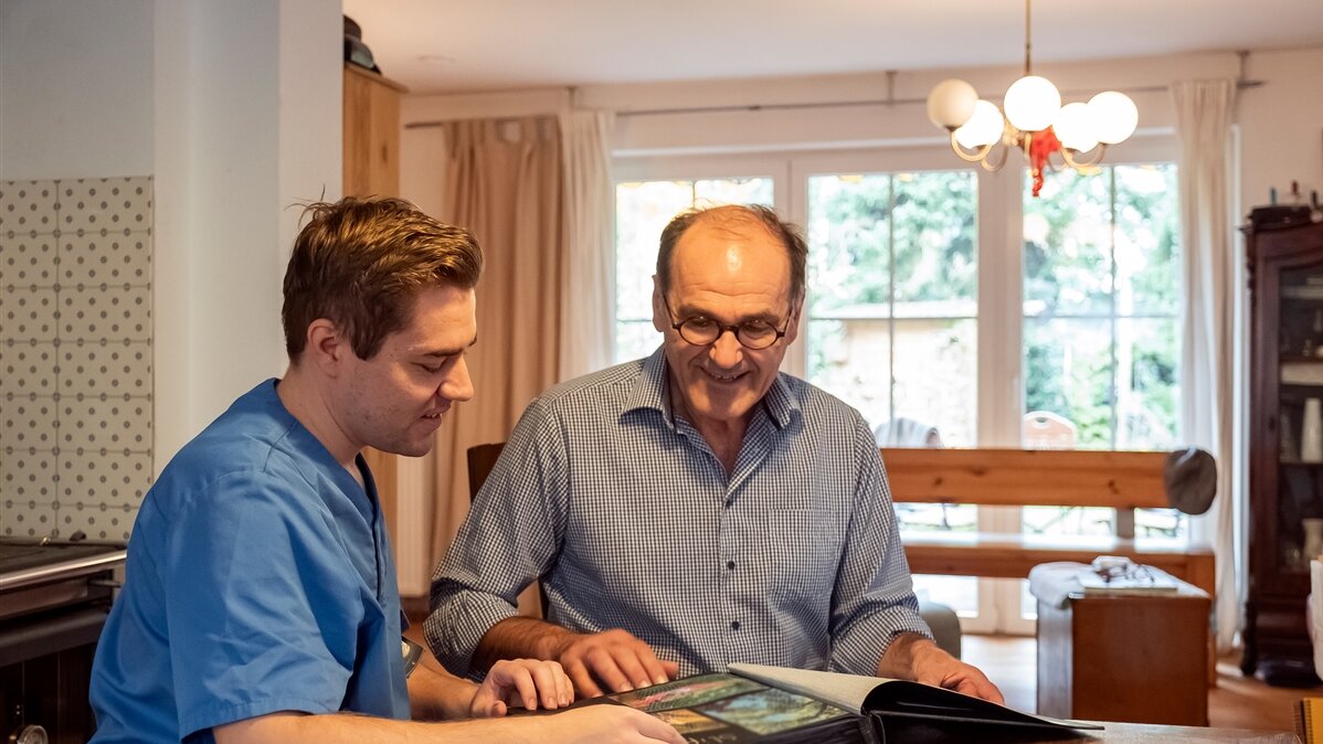 Ein junger Mann schaut sich mit einem älteren Mann ein Fotoalbum an.
