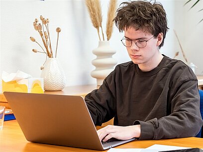 Ein junger Mann arbeitet an einem Laptop am Schreibtisch.