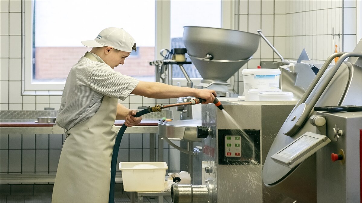 Stefan spritzt mit einem Schlauch Wasser auf eine Maschine.