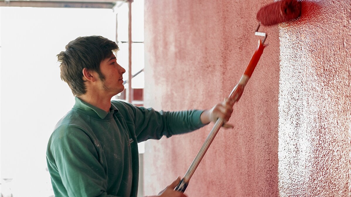 Ein Mann streicht die Wand mit einem Farbroller.