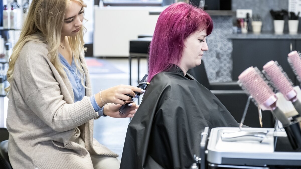 Ein junge Frau schneidet einer anderen jungen Frau die Haare.