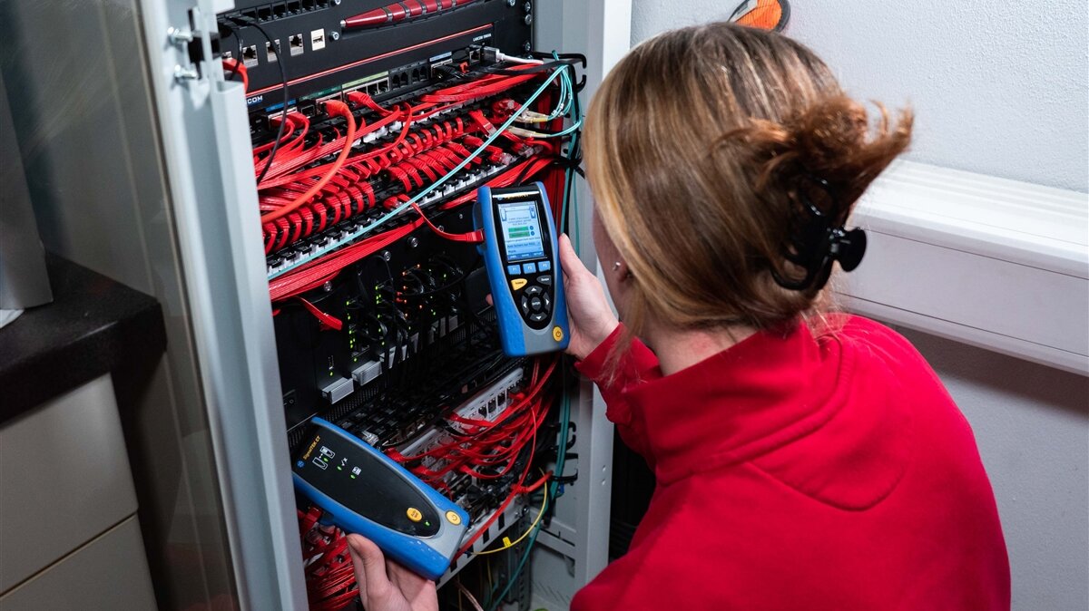 Eine Frau prüft Kabel eines Schaltkastens mit einem Spannungsmessgerät.