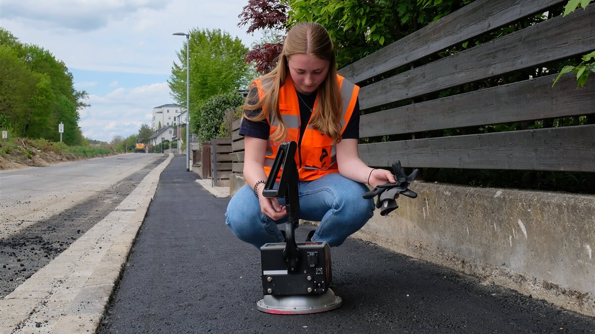 Anna misst mit einem Gerät die Verdichtung von frischem Asphalt.