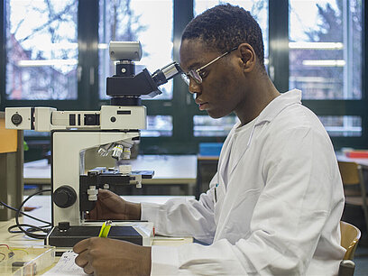 Ein junger Mann untersucht ein Objekt mit einem Mikroskop.