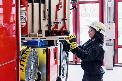 Eine Frau in Feuerwehrbekleidung schaut sich die Geräte in einem Feuerwehrfahrzeug an.