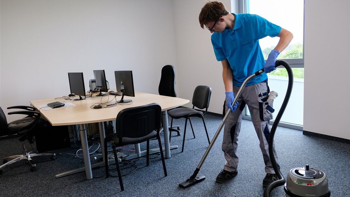Matthis saugt mit dem Staubsauger den Teppichboden in einem Büro.