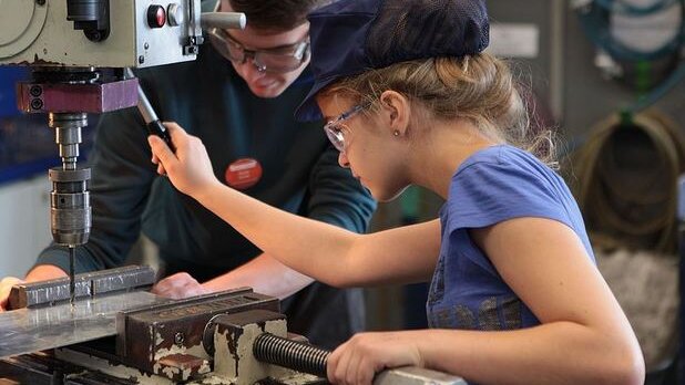 Ein Mädchen und ein Junge mit Sicherheitsbrille arbeiten an einer großen Bohrmaschine im MINT-Camp.