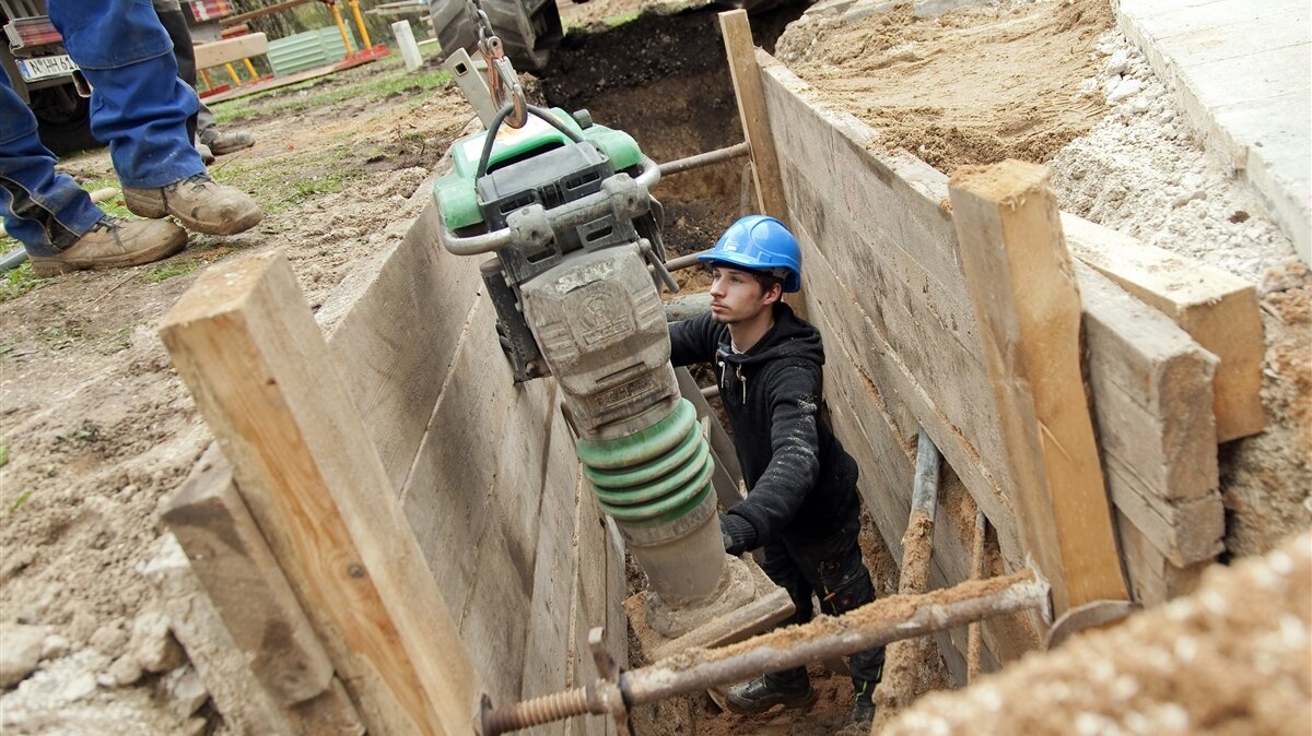 Ein junger Mann hält einen Presslufthammer in einer Baugrube.