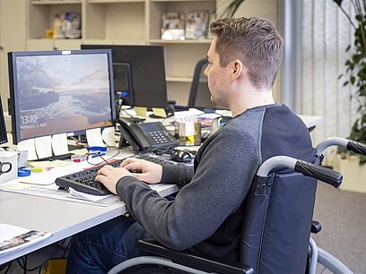 Ein junger Mann im Rollstuhl arbeitet am Computer.