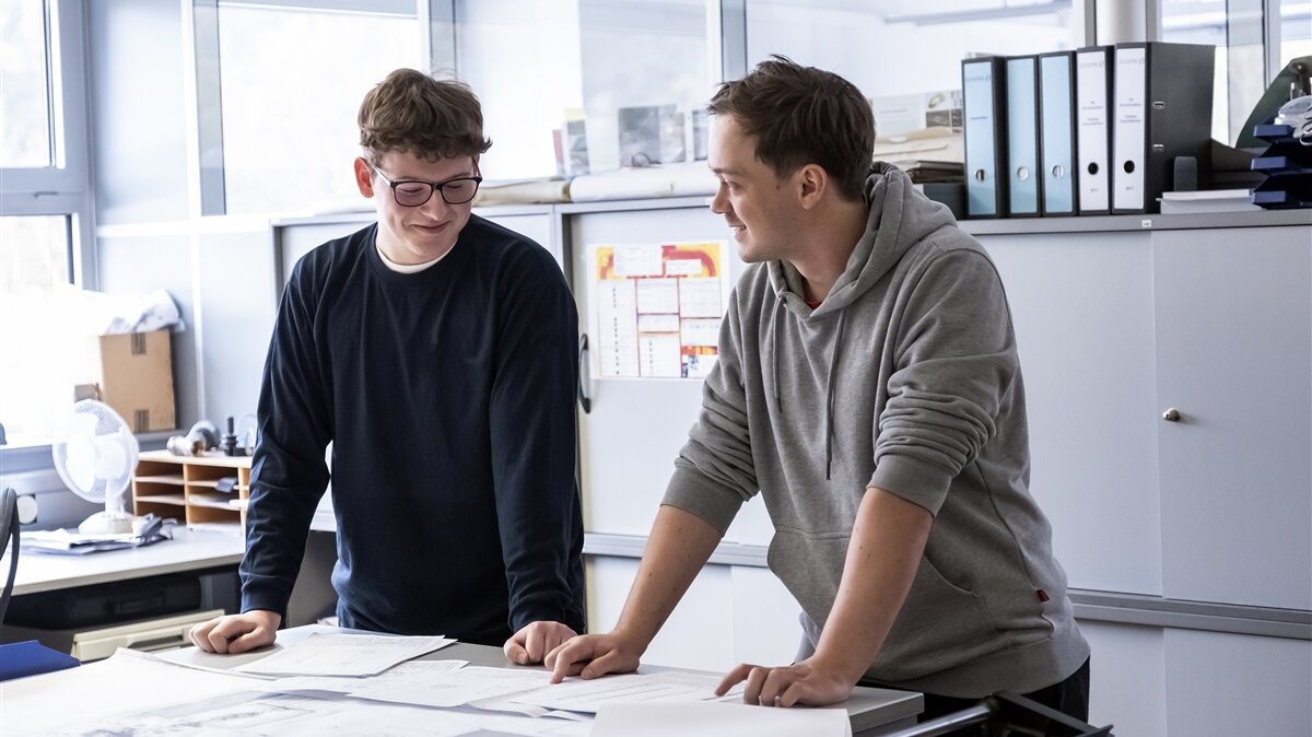 Zwei jungen Männer besprechen sich vor einem Bauplan